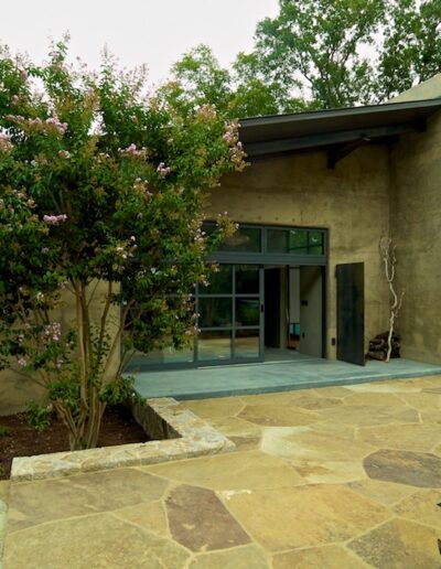 A modern single-story building with a patio area surrounded by natural landscaping.